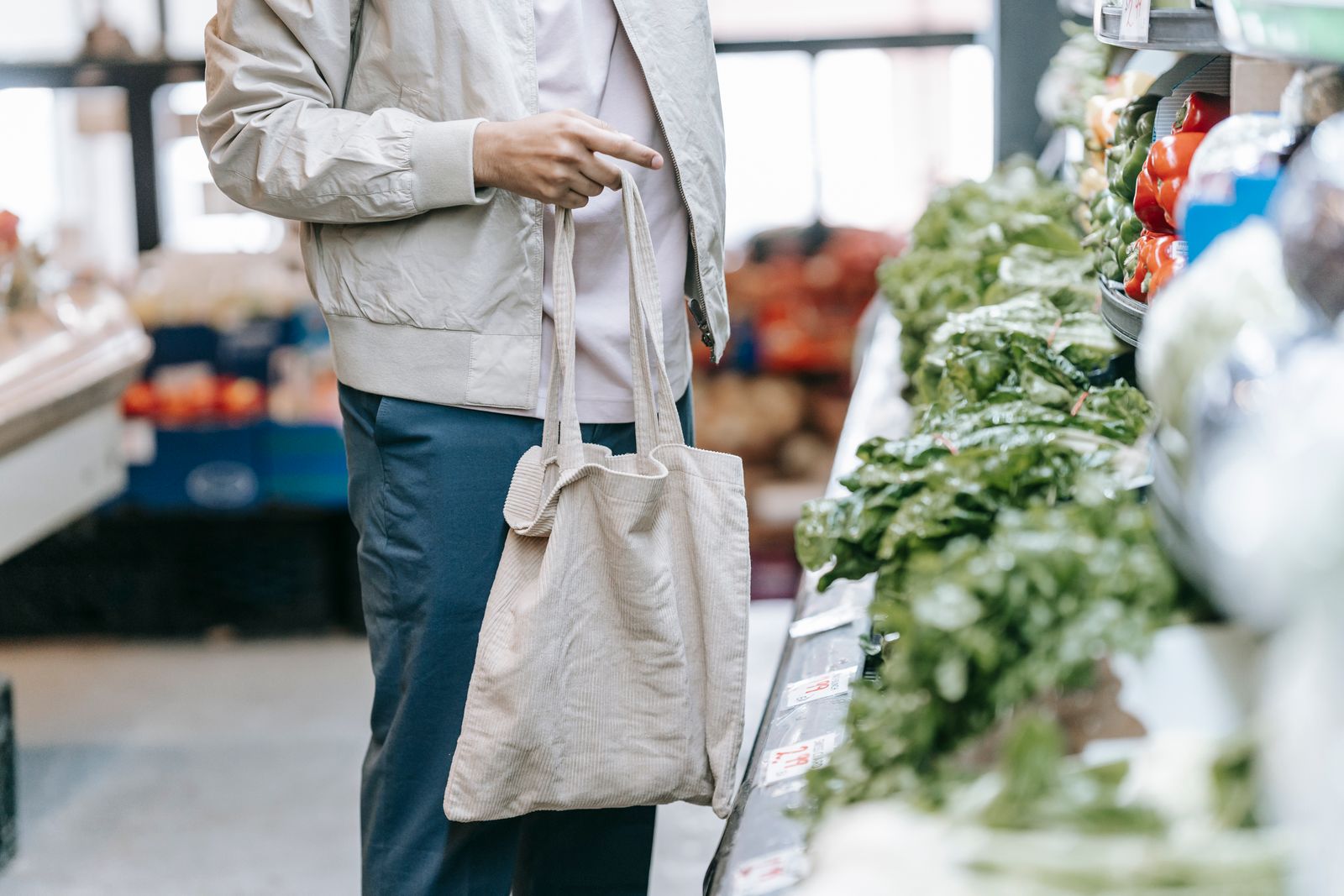 Persona con bolsa de tela ante un puesto de verduras frescas